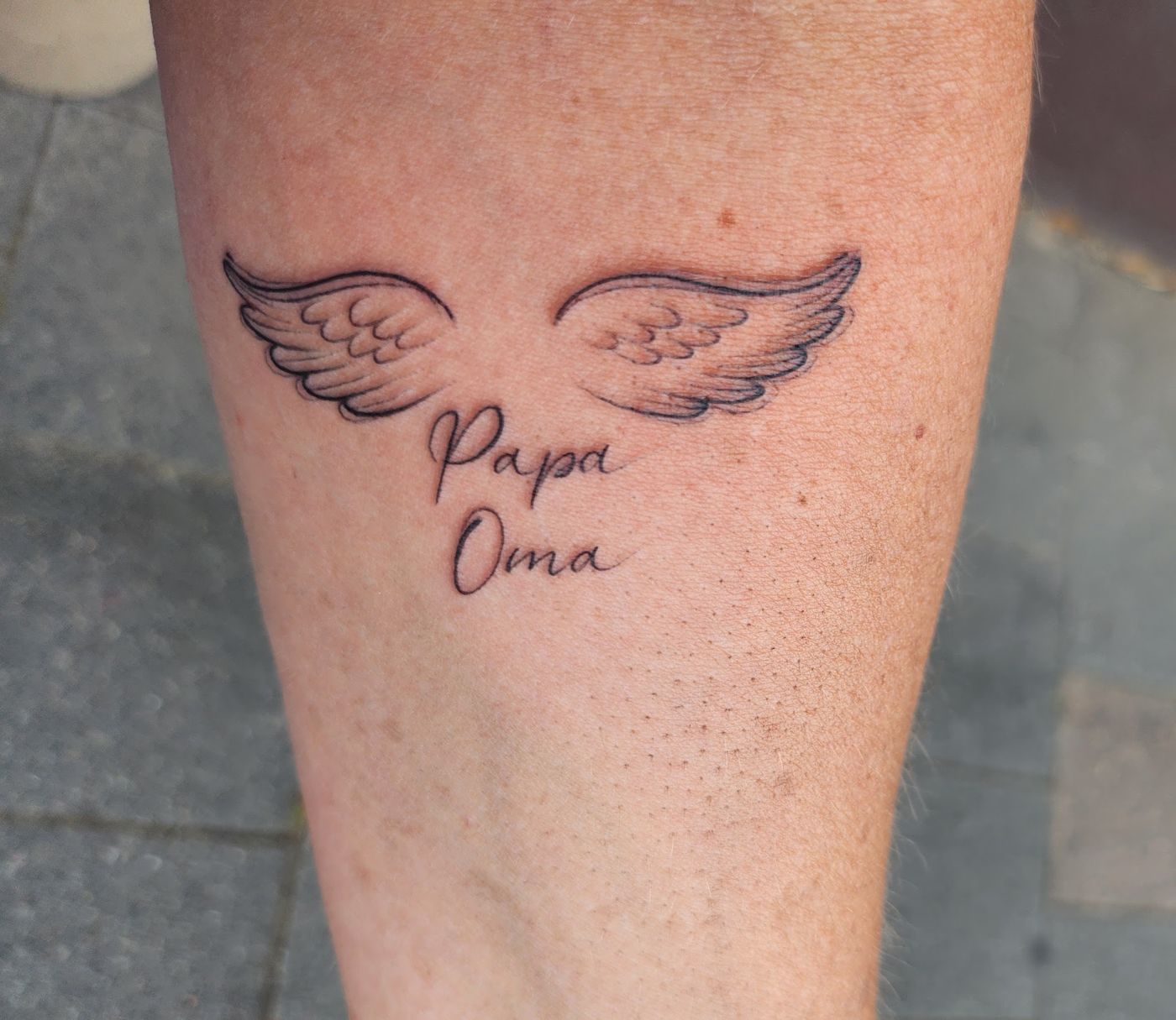 Tattoo mit Engelsflügeln und dem Schriftzug Papa Oma